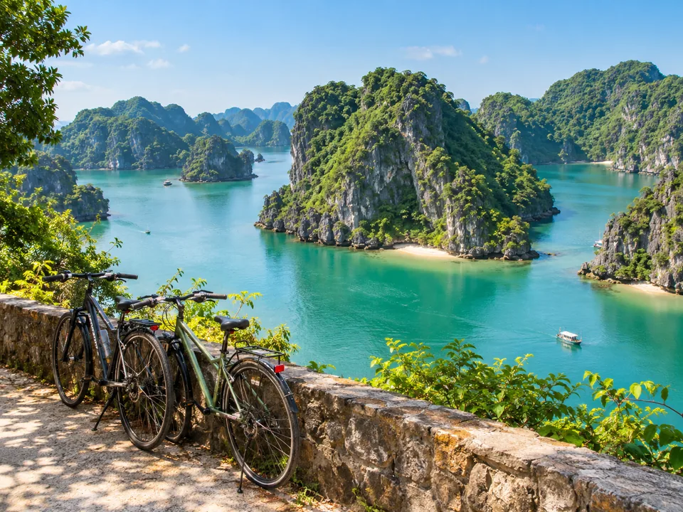Two bicycles leaning on a stone wall in a green valley ringed by karst hills