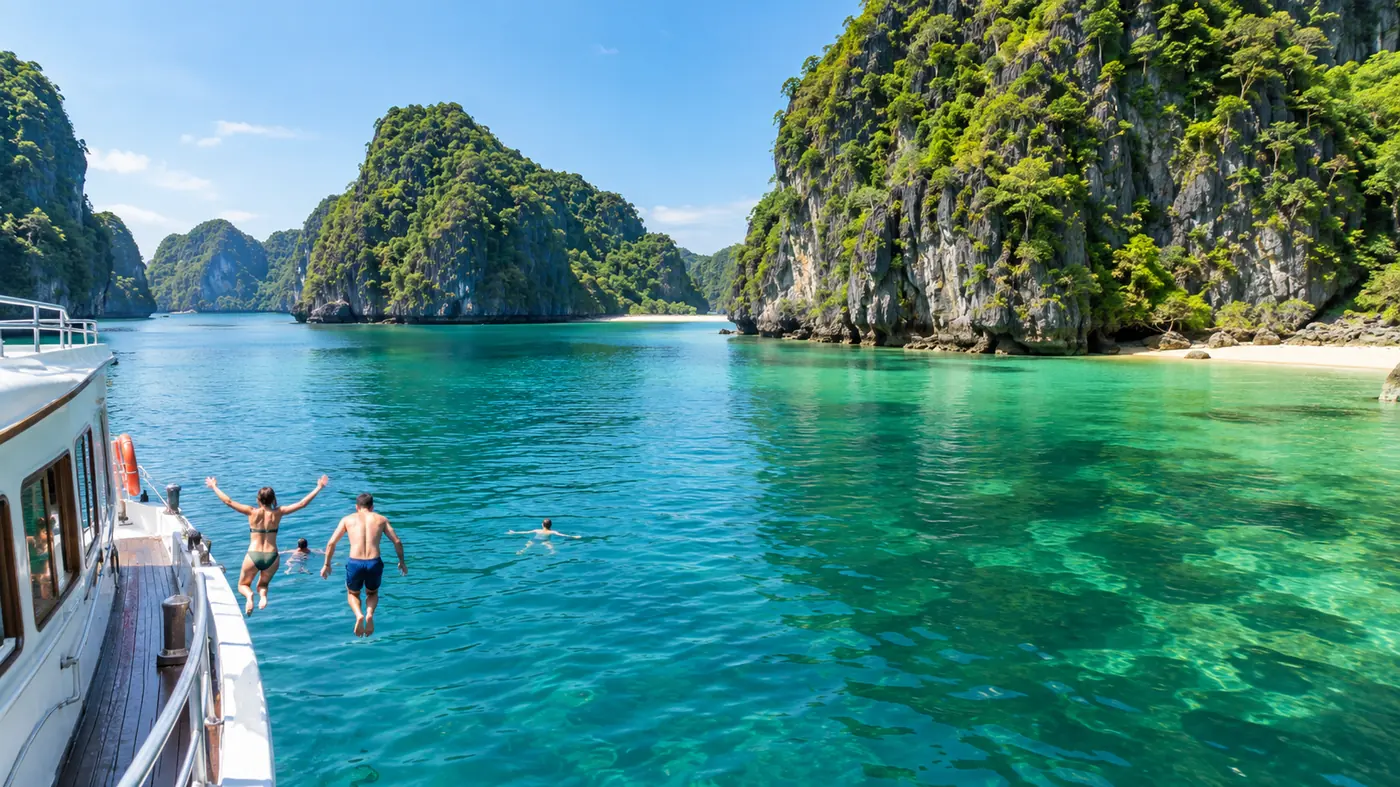 Swimmers jumping off a white day boat into clear emerald water beside a karst